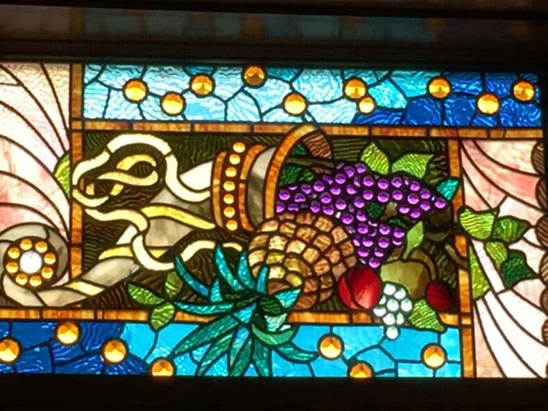Stained glass depicting a stylized animal alongside a cornucopia of fruits.