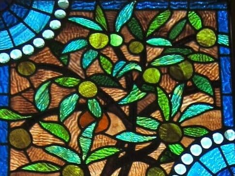 A colorful stained glass depiction of a leafy tree with green fruits.