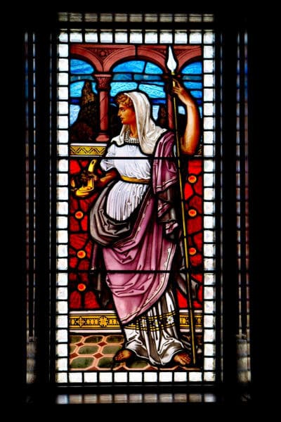 Stained glass depiction of a woman in classical attire holding a spear and a vessel.
